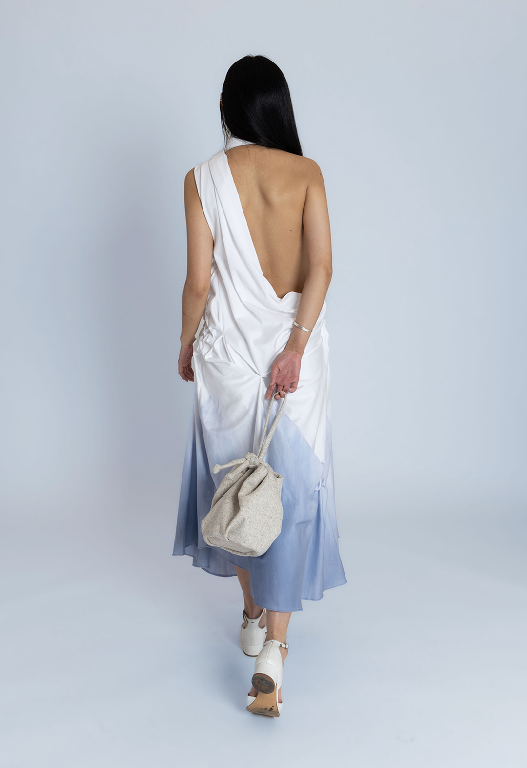 A model presents the back view of a white cotton dress dyed blue at the bottom.