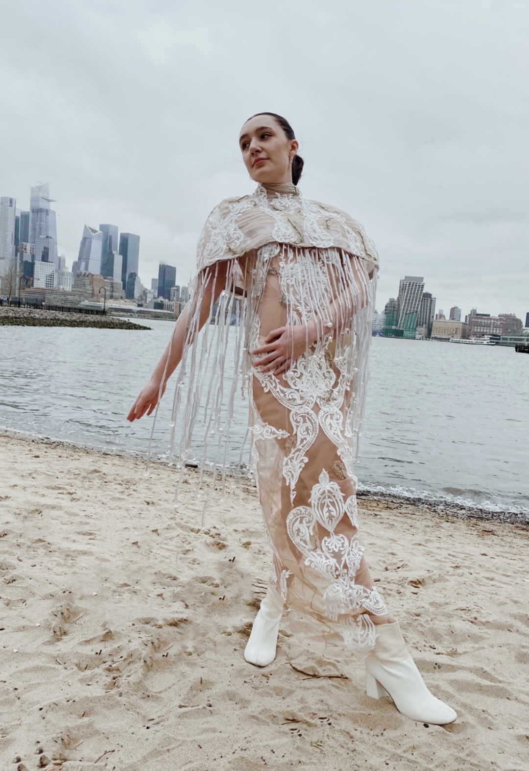 The garment is inspired by ocean pollution. Using recycled plastics and repurposed bridal fabrics, the look highlights waste in the fashion industry and beyond. The cape is modeled after a jelly fish, using beads that I created from plastic water bottles to make the tentacles. The ocean wave–inspired lace appliqués highlight the impact that waste has on our oceans and its creatures.