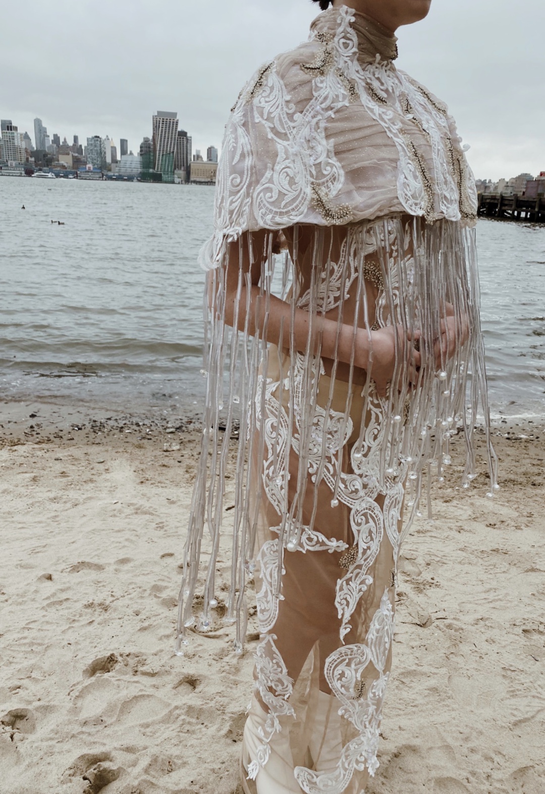 The garment is inspired by ocean pollution. Using recycled plastics and repurposed bridal fabrics, the look highlights waste in the fashion industry and beyond. The cape is modeled after a jelly fish, using beads that I created from plastic water bottles to make the tentacles. The ocean wave–inspired lace appliqués highlight the impact that waste has on our oceans and its creatures.