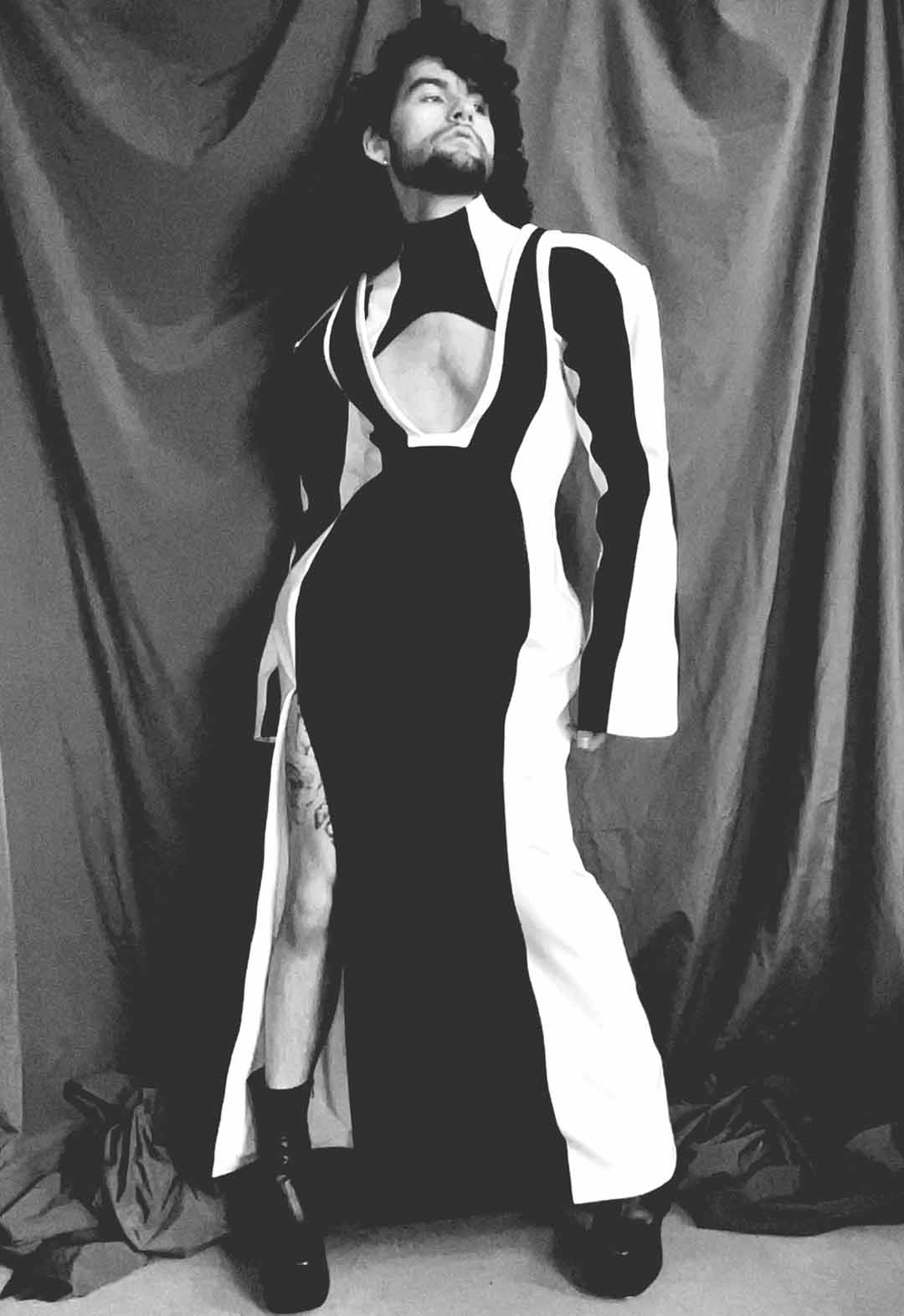 Photo of model wearing black and white color-blocked dress and yoke piece. A slit runs up one side of the garment, exposing the right leg. 
