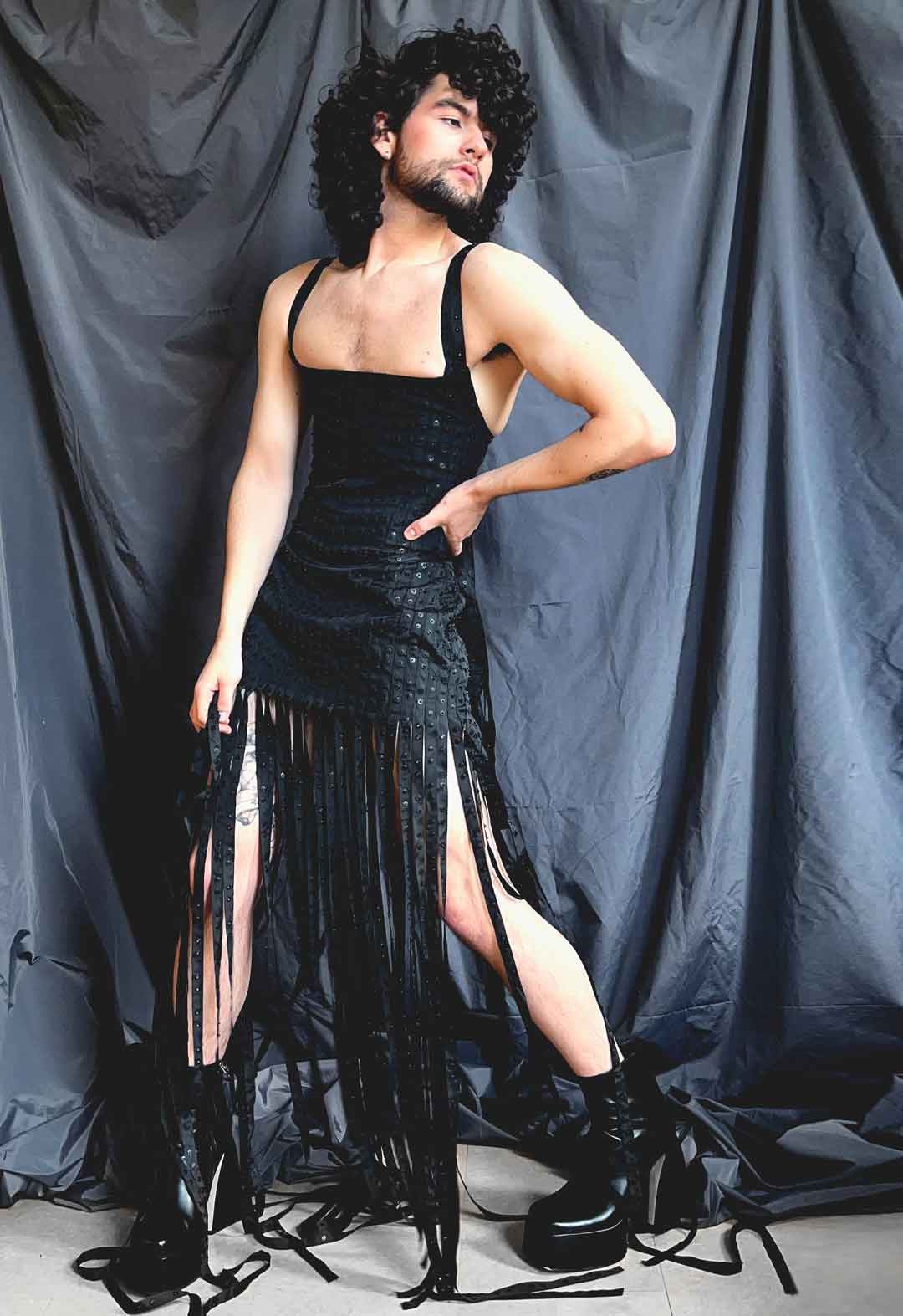 Three-quarter view of model wearing black corset and matching miniskirt. The textile is made of strips of snap-tape. The skirt has the snap-strip fringe at the hem and goes to the floor. 